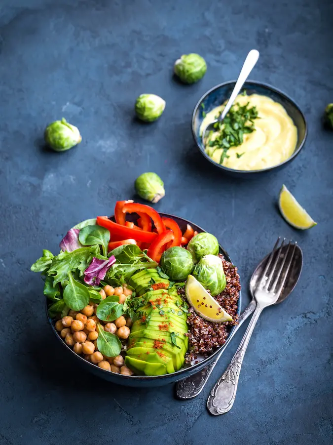 Dva veggie burgre s tmavočervenou plackou, zelenými listami, zapichnuté drevenými špajdlami na rustikálnej drevenej doske, s rozsypanými bylinkami na šedivom pozadí.