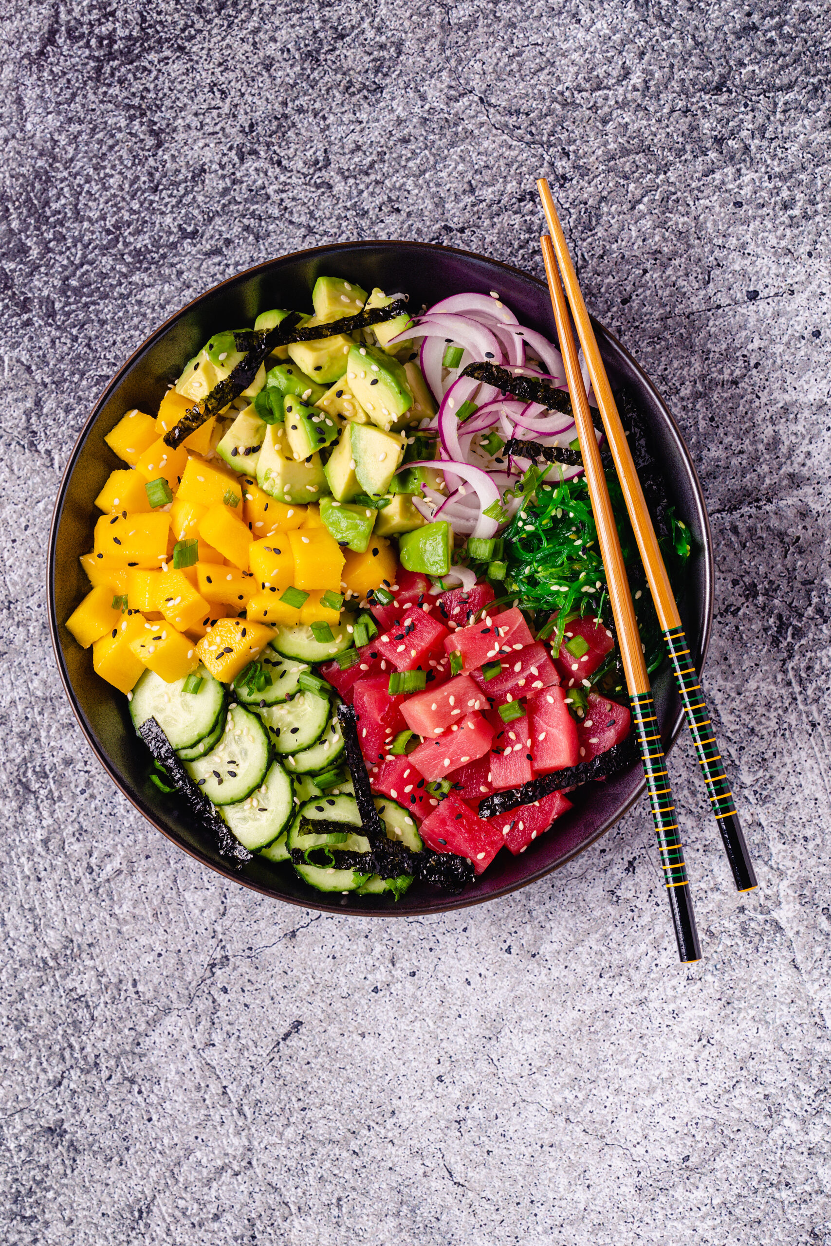 Burger so sezamovou žemľou, čerstvým šalátom, paradajkou a cibuľou na drevenej doske, do burgeru je zapichnutý nôž, v pozadí pohár tmavého nápoja a sivá utierka na tmavom pozadí.