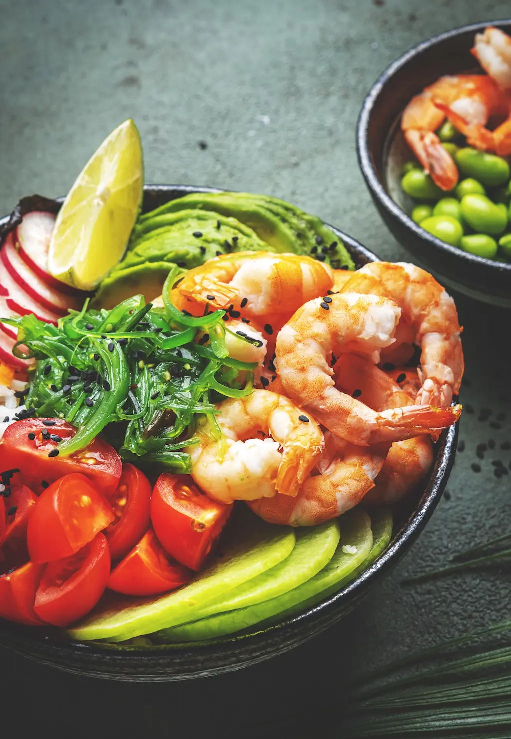 Surové hovädzie burgerové placky posypané zelenými bylinkami na čiernej kamennej doske, vedľa malá miska s červeným korenením, na texturovanom čiernom podklade.