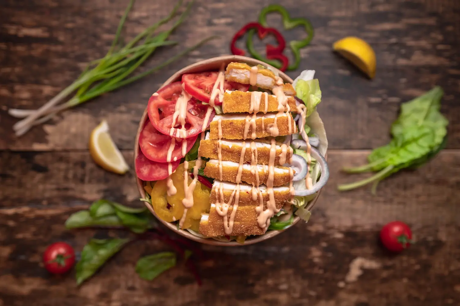 Vysoký dvojposchodový burger so sezamovou žemľou, syrom, slaninou a zelenými listami, na drevenom stole vedľa kopca hranolčekov, na tmavom pozadí.