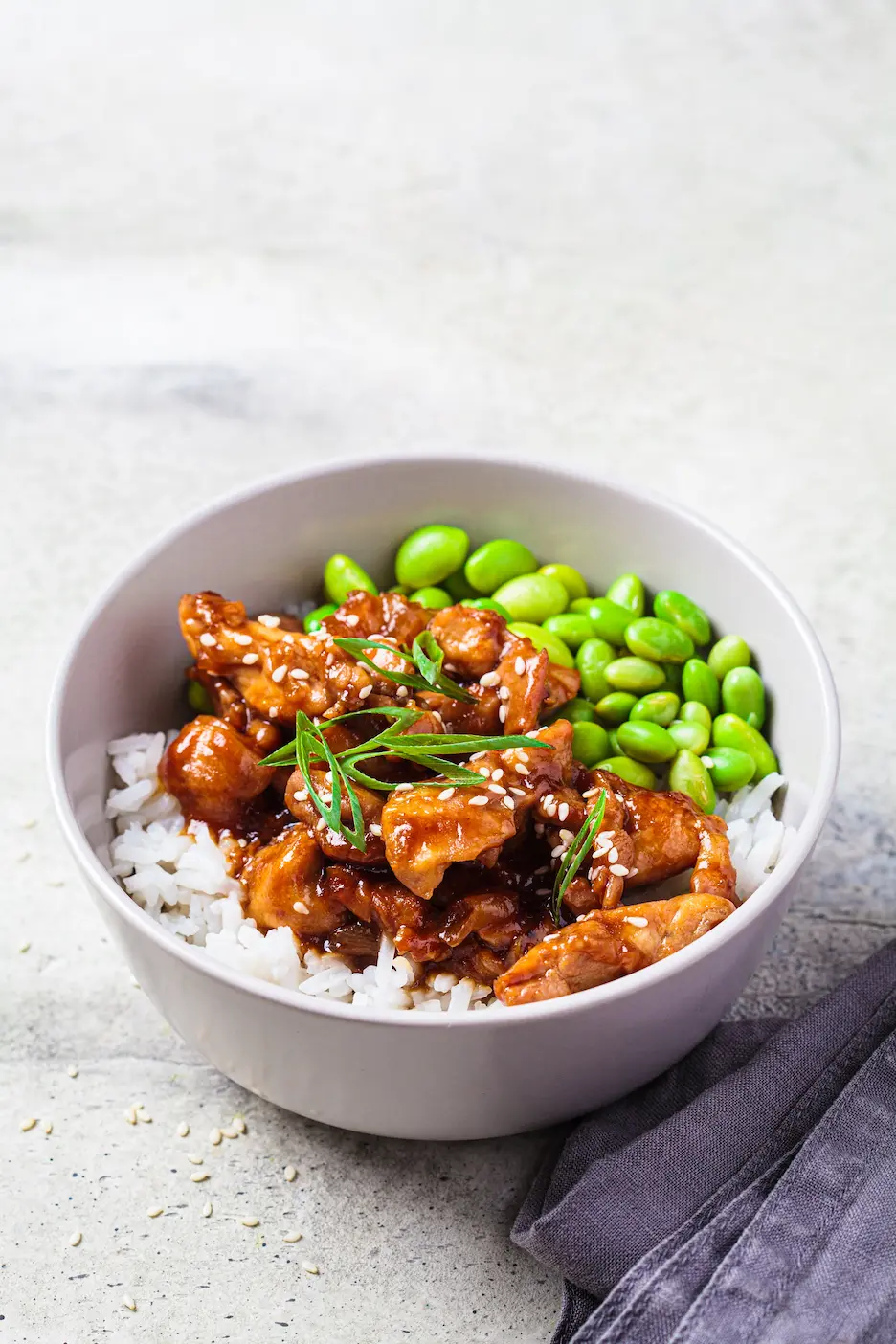 Vysoký dvojposchodový burger so sezamovou žemľou, syrom, slaninou a zelenými listami, na drevenom stole vedľa kopca hranolčekov, na tmavom pozadí.